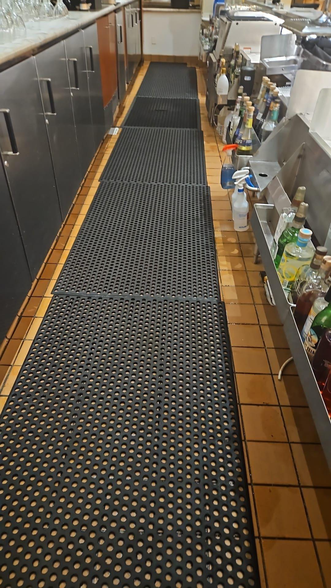 Bar counter with rubber floor mats and various bottles and supplies.